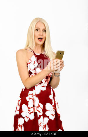 Donna attraente nel grazioso vestito estivo con un espressione sconvolta mentre utilizzando il suo telefono cellulare, presa contro uno sfondo bianco Foto Stock