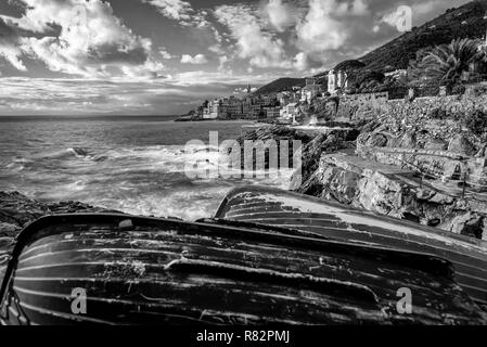 In bianco e nero di scena spiaggiata in legno barche da pesca in inverno sulla costa rocciosa di Bogliasco, Italia sulla costa ligure Foto Stock