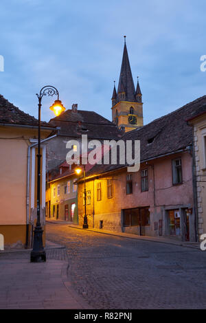 Tipiche pietre ciottoli street della città di Sibiu Romania, con case colorate, campanile e la luce post Foto Stock
