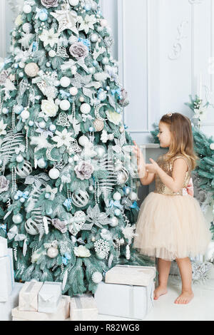 Bambina nel bel vestito decora l'albero di Natale. Foto Stock