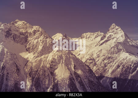 Ripide cime delle montagne del Caucaso nella zona del villaggio di Dombay. Immagine dai toni di colore viola Foto Stock