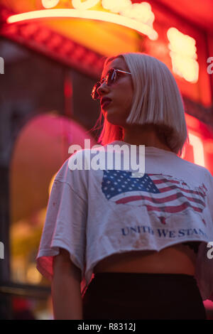 Ritratto cinematografico della ragazza bionda con il bianco di t-shirt e bandiera americana sul segno al neon di notte Foto Stock