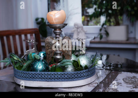 La disposizione dei rami di abete, di color turchese albero di Natale le sfere, le renne e le candele titolari di legno con ali d'angelo in piedi nella sala da pranzo. Foto Stock