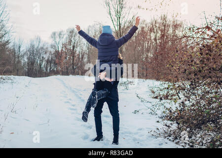 Guy holding e sollevamento della sua fidanzata in mani in inverno foresta. Ragazza dei bracci di sollevamento. Le persone felici avendo divertimento all'aperto Foto Stock