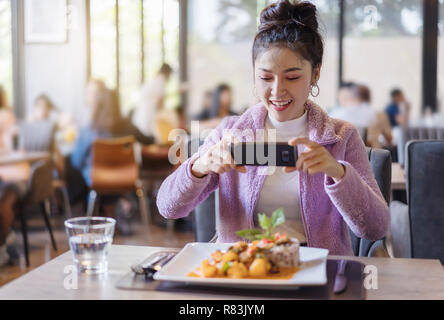 Donna che utilizza smartphone prendere le foto di cibo prima di mangiare nel ristorante Foto Stock