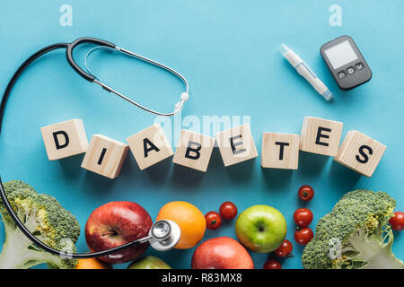 'Diabetes' scritte fatte di cubi di legno con attrezzature mediche e frutti su sfondo blu Foto Stock