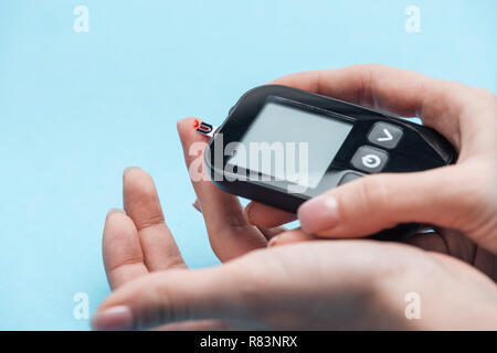 Vista ritagliata della mani femminili test del livello di glucosio con il glucometro su sfondo blu Foto Stock