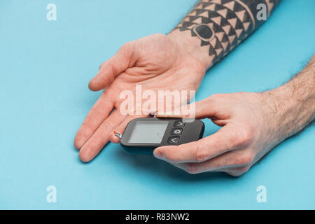 Vista ritagliata dell'uomo facendo a livello di glucosio il test con il glucometro su sfondo blu Foto Stock
