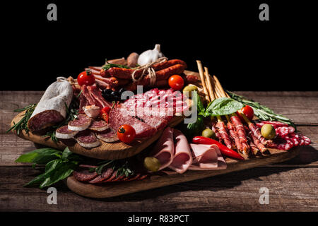 Schede di taglio con deliziosi salami, salsicce affumicate, prosciutto, le verdure e le erbe in legno tavolo rustico Foto Stock