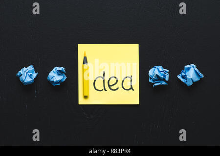 "Idea" parola scritta sul foglietto adesivo blu e carta sgualcita palle su sfondo nero, idee concetto Foto Stock