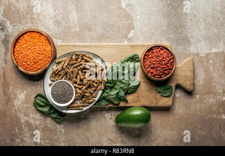 Vista dall'alto di un sano muesli, goji bacche, di lenticchie rosse e spinaci su tavola di legno con sfondo rustico Foto Stock