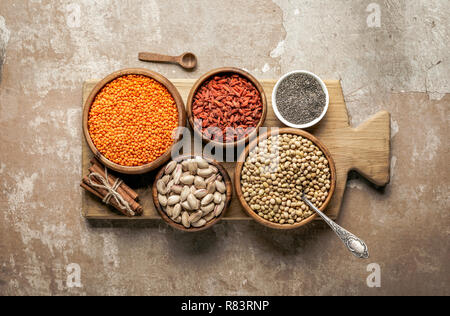 Vista superiore della tavola di legno con legumi, goji bacche ingredienti sani e con sfondo rustico Foto Stock
