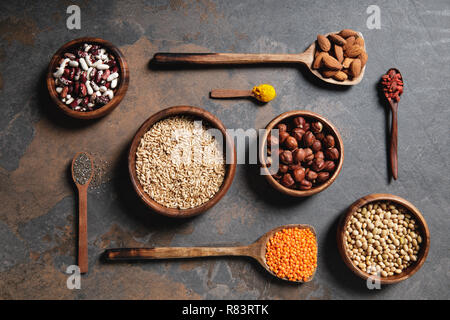 Vista dall'alto di ciotole di legno e cucchiai con superfoods, legumi e cereali sul tavolo Foto Stock