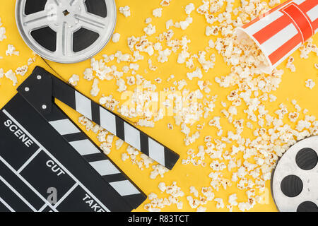 Bobine di pellicola, clapperboard e ribaltata benna a strisce con popcorn isolato su giallo Foto Stock