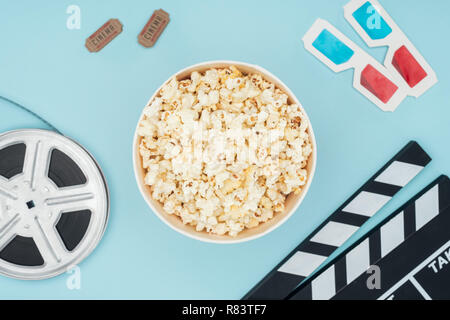 Vista superiore della clapperboard, bobina di pellicola, occhiali 3d, i biglietti del cinema e popcorn isolato della benna su blu Foto Stock