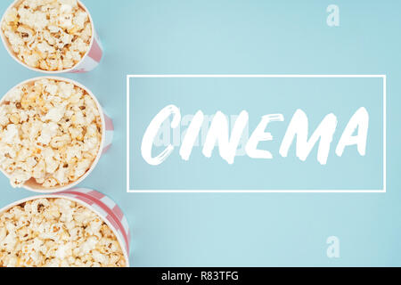 Vista superiore di cestelli con popcorn in fila verticale e 'cinema' lettering isolato su blu Foto Stock