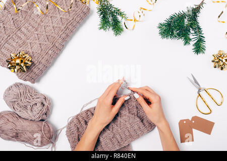 Vista da sopra la donna con le mani in mano per maglieria maglione di lana con aghi fra laici piana golden decorazioni di Natale e rami di alberi di abete su bianco tabl Foto Stock