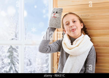 Bambino ragazza è seduta su un davanzale e giocare con il guanto fatti a mano. Bella vista al di fuori della finestra - giornata di sole in inverno e neve. Foto Stock