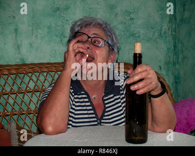 Un senior donna con una bottiglia di vino e un gran numero di pillole in mano di diversi colori e dimensioni Foto Stock