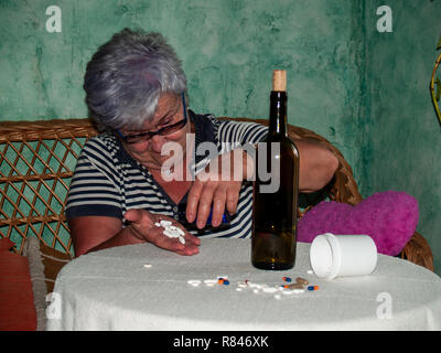 Un senior donna con una bottiglia di vino e un gran numero di pillole in mano di diversi colori e dimensioni Foto Stock