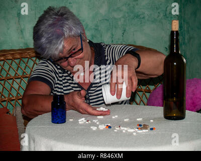 Un senior donna con una bottiglia di vino e un gran numero di pillole in mano di diversi colori e dimensioni Foto Stock