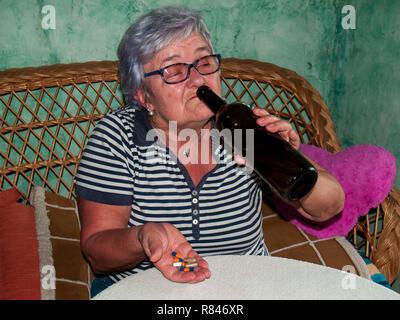 Un senior donna con una bottiglia di vino e un gran numero di pillole in mano di diversi colori e dimensioni Foto Stock
