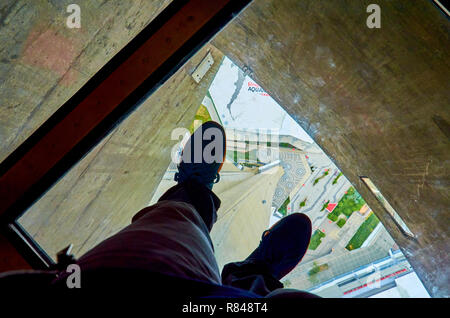 L'uomo con i piedi sul pavimento di vetro della CN tower, 350 metri sopra il livello del suolo. I visitatori sono ammessi a camminare o strisciare attraverso il pavimento di vetro. Foto Stock