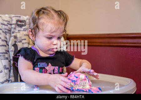 Un anno vecchia ragazza scoprire quanto è divertente giocare in una torta di compleanno. (MR) Foto Stock