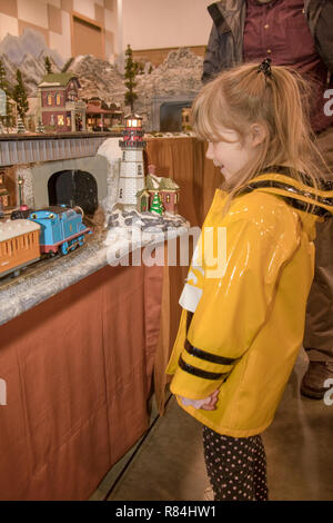 Quattro anni di ragazza con un impermeabile giallo, guardando un modello di treno village presso il treno show. Foto Stock