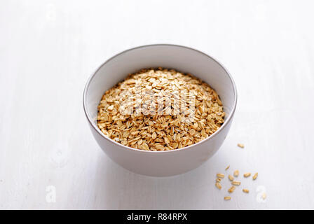 Bianco di ceramica ciotola di farina d'avena a secco su sfondo bianco con un'ombra, visualizzate in primo piano da un angolo alto Foto Stock