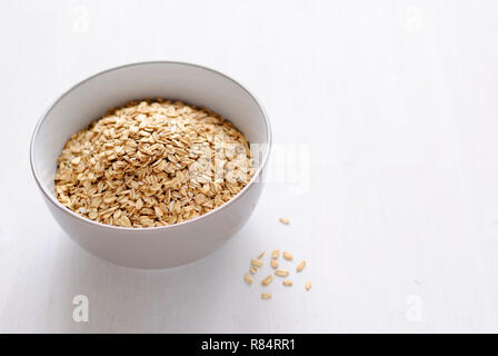 Bianco di ceramica ciotola di farina d'avena a secco su sfondo bianco con un'ombra, visualizzate in primo piano da elevato angolo con spazio di copia Foto Stock