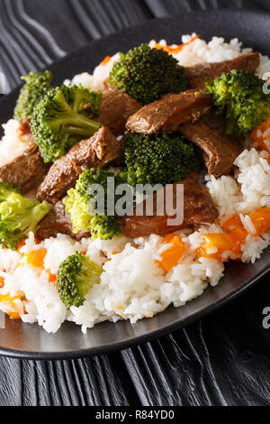 Carni bovine con broccoli, riso e persimmon close-up su una piastra sul piano verticale. Foto Stock