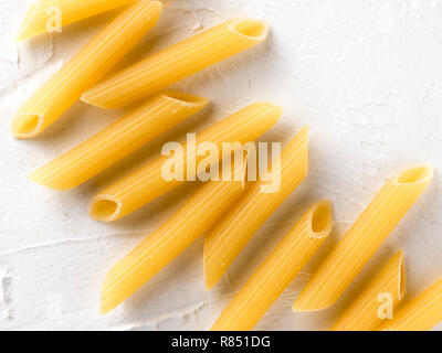 La pasta grezza come sfondo di cibo. Italian Penne Rigate Maccheroni testurizzato su sfondo bianco. La pasta secca selezione vicino. Vista superiore o laici piatta con spazio di copia Foto Stock