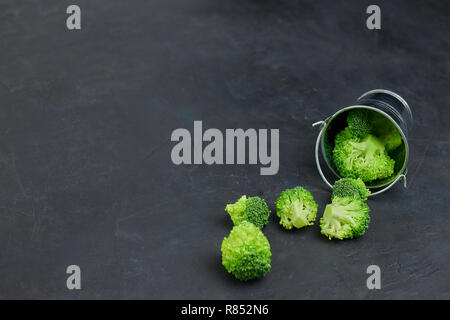 Placer broccoli verdi segmenti da un piccolo cucchiaio. Mangiare sano pattern su sfondo scuro. Spazio Copia vista dall'alto. Cibo vegetariano. Foto Stock