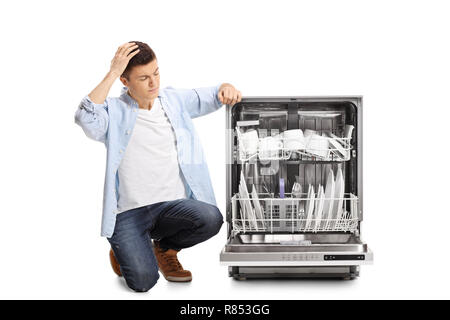 Arrabbiato giovane ragazzo inginocchiato accanto ad una lavastoviglie caricato tenendo la sua testa isolata su sfondo bianco Foto Stock