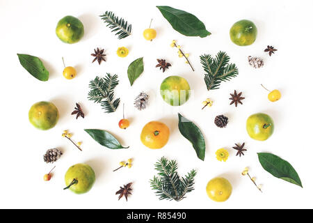 Natale composizione in stile. Tangerine agrumi e foglie, Abete rami, anice stelle, agrifoglio Bacche e piccola mele sul tavolo bianco sullo sfondo. Vacanze inverno pattern. Appartamento laico, vista dall'alto. Foto Stock