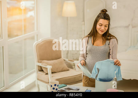 Le emozionanti aspettativa. Il Sorridente donna incinta tenendo i bambini vestiti Foto Stock