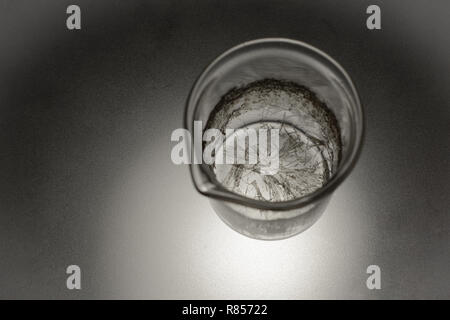 Vetro chimica con cristalli di acido salicilico su un vetro opaco con retroilluminazione da sotto Foto Stock