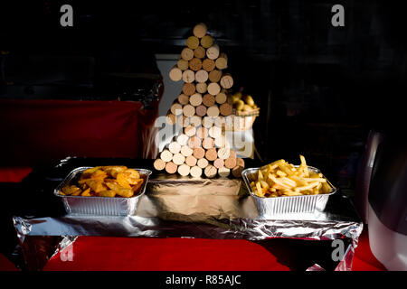 Il fast food stand ad una fiera di Natale in Francia, visualizza 2 di stagnola contenitori con diversi tipi di chip handcut accanto a albero di natale costruito da tappi di sughero Foto Stock