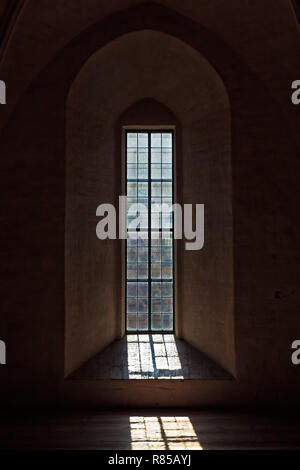 La luce entra attraverso la vecchia finestra del castello medievale di Turku, Finlandia. La griglia della finestra crea un interessante ombra sul pavimento. Foto Stock
