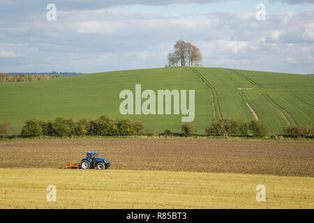 Un trattore coltiva il campo sottostante Brightwell Barrow, Età del Bronzo ciotola Barrow sulla collina accanto a Wittenham Clumps, Oxfordshire. Foto Stock