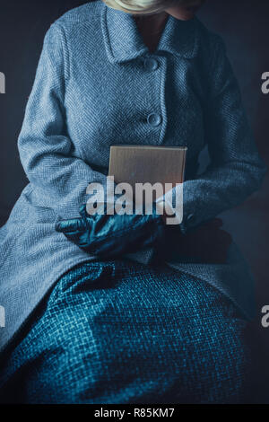 Donna storico in cappotto invernale in possesso di un libro Foto Stock