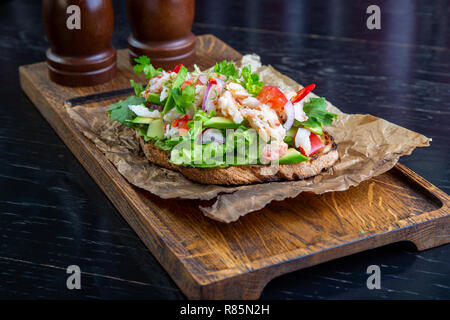 Deliziose bruschette con polpa di granchio nel ristorante dello sfondo. Esclusiva sano cibo servito su una tavola di legno e carta craft Foto Stock