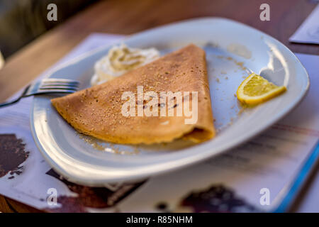 Poco profonda selettiva di messa a fuoco di una deliziosa crêpe pancake europeo, nella piastra bianca servita in stile greco con lo zucchero di canna e la fetta di limone e creme in s Foto Stock