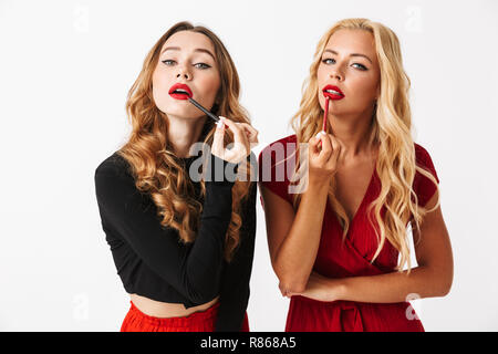 Ritratto di due giovani graziosi elegantemente vestito donne che indossano il trucco in piedi isolato su sfondo bianco, facendo il loro trucco Foto Stock