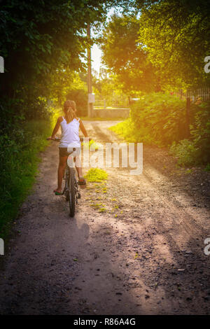Ragazza felicemente in sella ad una bicicletta su un territorio rurale strada sterrata Foto Stock