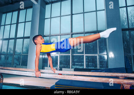 Il ragazzino è impegnata nella ginnastica sport su barre parallele in palestra. Le prestazioni, sport, acrobat acrobatico, esercizio, il concetto di formazione Foto Stock