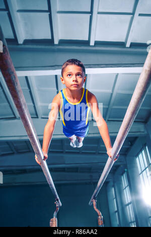 Il ragazzino è impegnata nella ginnastica sport su barre parallele in palestra. Le prestazioni, sport, acrobat acrobatico, esercizio, il concetto di formazione Foto Stock