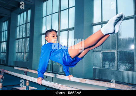 Il ragazzino è impegnata nella ginnastica sport su barre parallele in palestra. Le prestazioni, sport, acrobat acrobatico, esercizio, il concetto di formazione Foto Stock