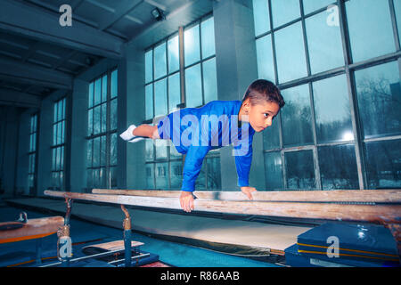 Il ragazzino è impegnata nella ginnastica sport su barre parallele in palestra. Le prestazioni, sport, acrobat acrobatico, esercizio, il concetto di formazione Foto Stock